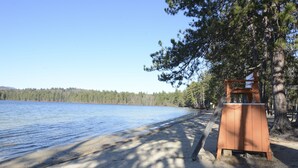 A sandy beach with a wooden structure, likely a lifeguard stand, near a calm lake surrounded by trees.