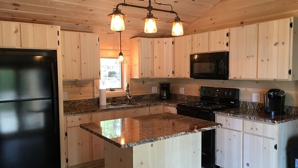 A modern kitchen with wooden cabinets, a granite countertop, a black refrigerator, a microwave, and a stove.
