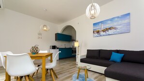Ein modernes Wohnzimmer mit einem schwarzen Sofa, weißen Stühlen, einem Glastisch und einem Essbereich mit einem Holztisch und Stühlen.