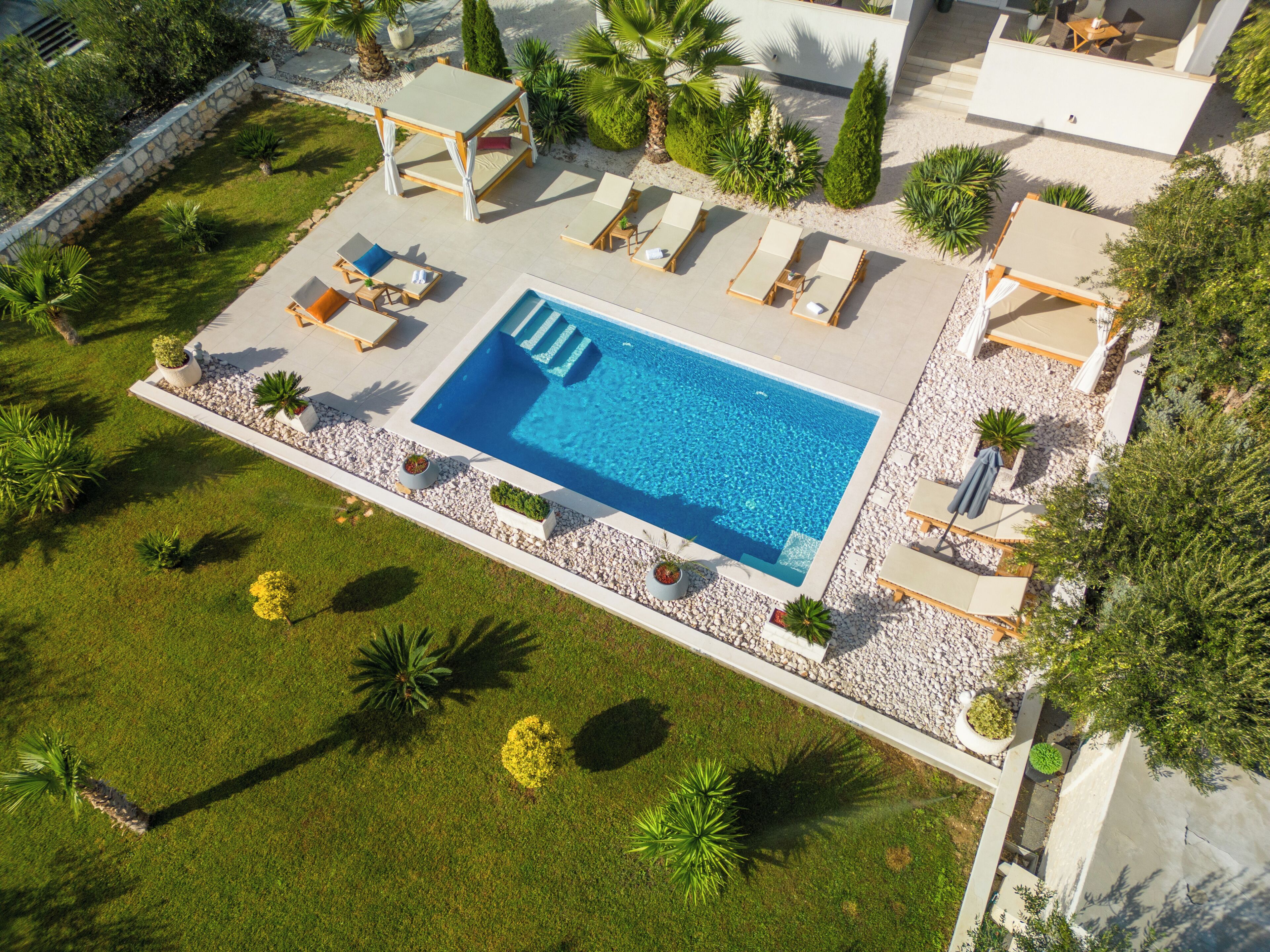 Une piscine entourée de chaises longues, elle-même bordée d’un jardin aménagé avec différentes espèces de plantes et d’un mur en pierre.