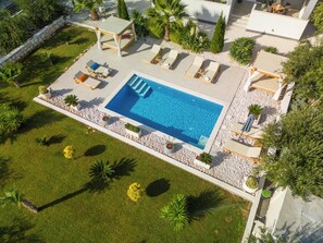 Ein Swimmingpool mit Liegestühlen, umgeben von einem angelegten Garten mit verschiedenen Pflanzen und einer Steinmauer.