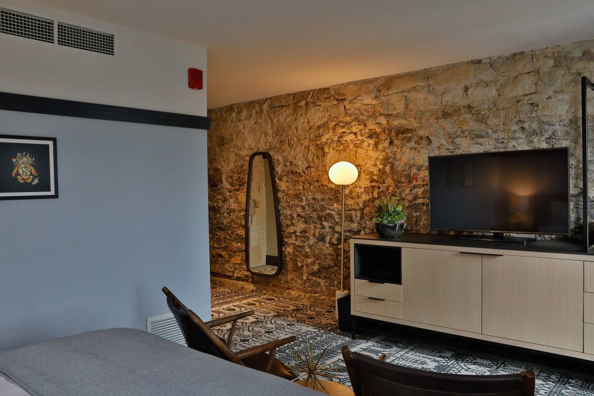 A modern room with a stone wall, a flat-screen TV, a wooden cabinet, and a patterned rug.