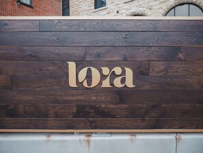 A wooden wall with the name "lora" carved in a stylized font.