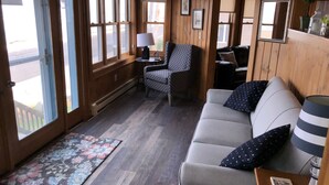 Una habitación acogedora con detalles de madera, un sofá, un sillón estampado, una mesita de noche con lámpara y una alfombra.