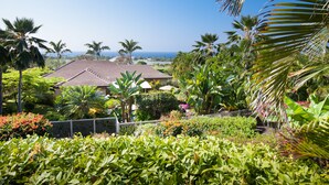 A tropical garden with a house, palm trees, and a view of the ocean. - 5 ★ Nakukui Hale: Waterfall Pool, Gazebo & Ocean Views, Gated Kona Town Retreat (Kailua-Kona)