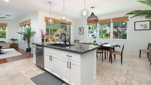 A spacious kitchen with a central island, large windows with views of greenery, and modern pendant lighting. - 5 ★ Nakukui Hale: Waterfall Pool, Gazebo & Ocean Views, Gated Kona Town Retreat (Kailua-Kona)
