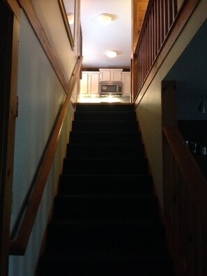 Stairs lead to a kitchen with white cabinets and a microwave.