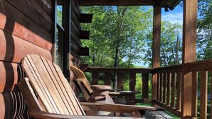 Una terraza de madera con sillas de descanso y una mesa, rodeada de un cerco de madera y árboles.