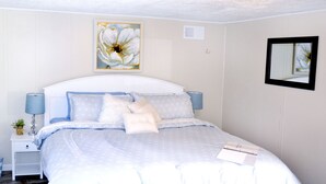 Un dormitorio ordenado con cama, mesitas de noche, lámpara y un espejo en la pared.