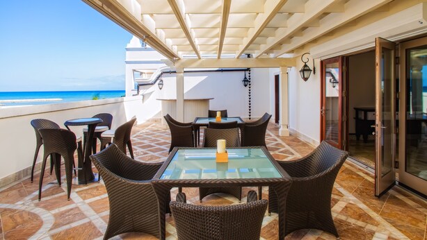 An outdoor patio with a glass table and wicker chairs, overlooking a beach. - Cap Cana Oceanfront Penthouse Marina Apartment, Sleeps 10, overlooks ocean (Punta Cana)