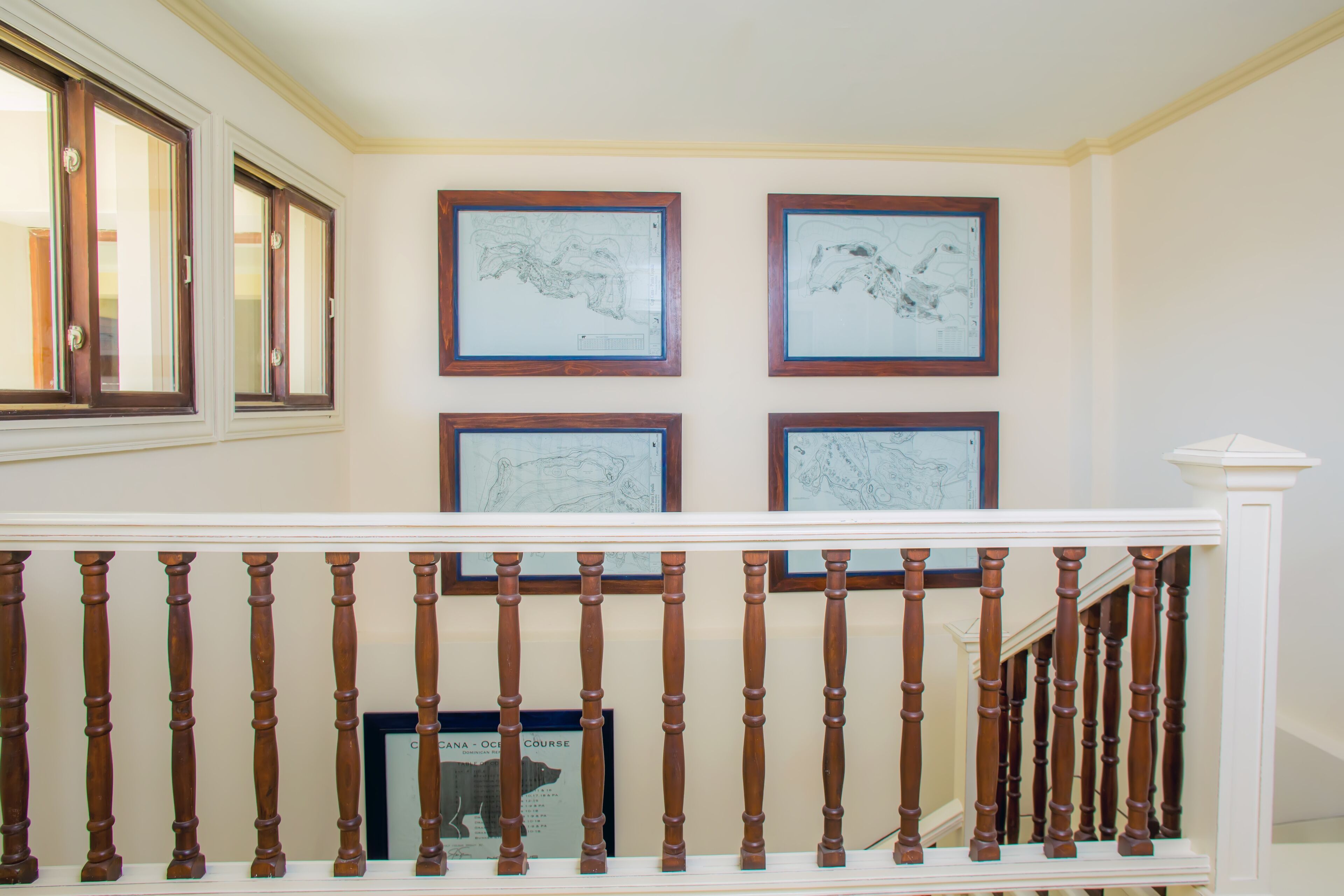 Una escalera con balaustres de madera y barandilla blanca, que conduce a un rellano con cuatro mapas enmarcados en la pared.