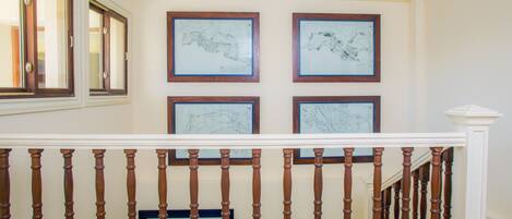 Una escalera con balaustres de madera y barandilla blanca, que conduce a un rellano con cuatro mapas enmarcados en la pared.