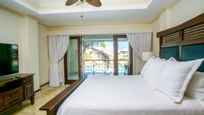 A hotel room with a large bed, a ceiling fan, a TV, and a view of a pool and palm trees. - Cap Cana Oceanfront Penthouse Marina Apartment, Sleeps 10, overlooks ocean (Punta Cana)