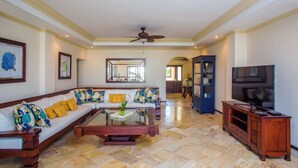 A spacious living room with a sectional sofa, a coffee table, a television, and a ceiling fan. - Cap Cana Oceanfront Penthouse Marina Apartment, Sleeps 10, overlooks ocean (Punta Cana)