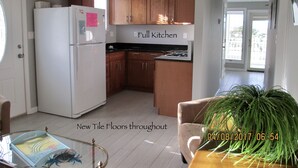 A modern kitchen with wooden cabinets, a white refrigerator, and a black countertop. There is a potted plant in the corner and a glass coffee table with a crab design. - LAVALLETTE New Panoramic Deck, Outdoor shower, and Kitchen INCLUDES BEACH BADGES (Lavallette)