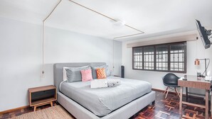 A modern bedroom with a large bed, a desk, and a window with bars.
