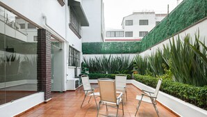 A courtyard with a tiled floor, white walls, and a green vertical garden. There are four white chairs arranged around a small table.