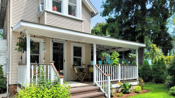 A two-story house with a covered porch, a front door, and a small outdoor seating area with a table and chairs.