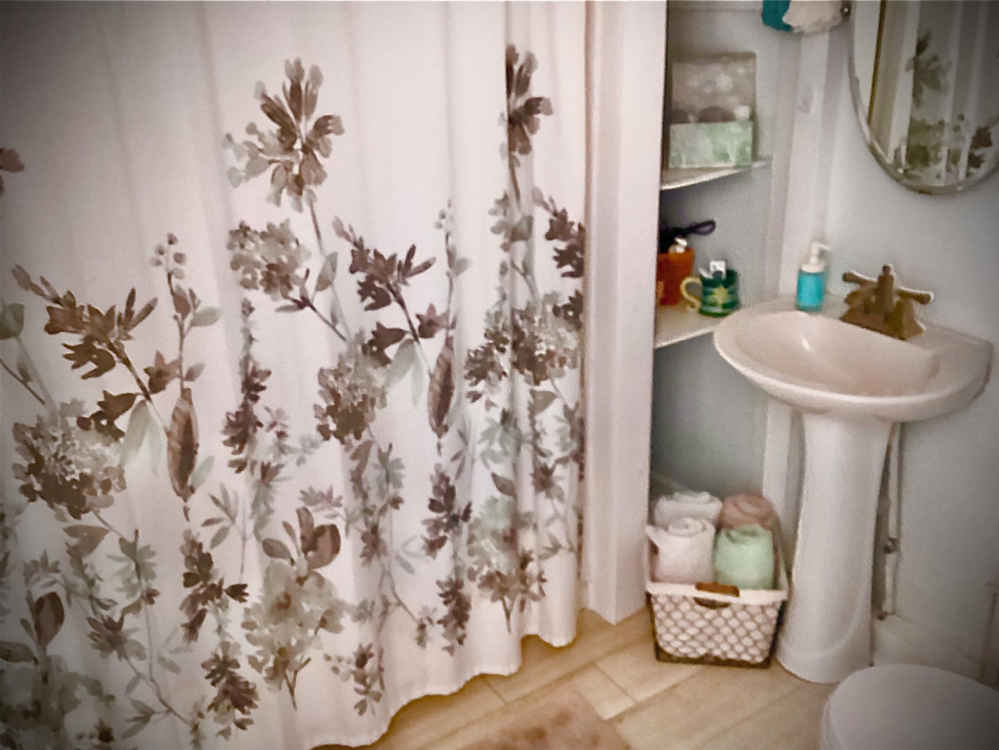 A bathroom with a floral shower curtain, a sink, and a small storage basket.