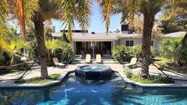 Una piscina azul cristalina con un jacuzzi en el centro, rodeada de palmeras y sillas de descanso.