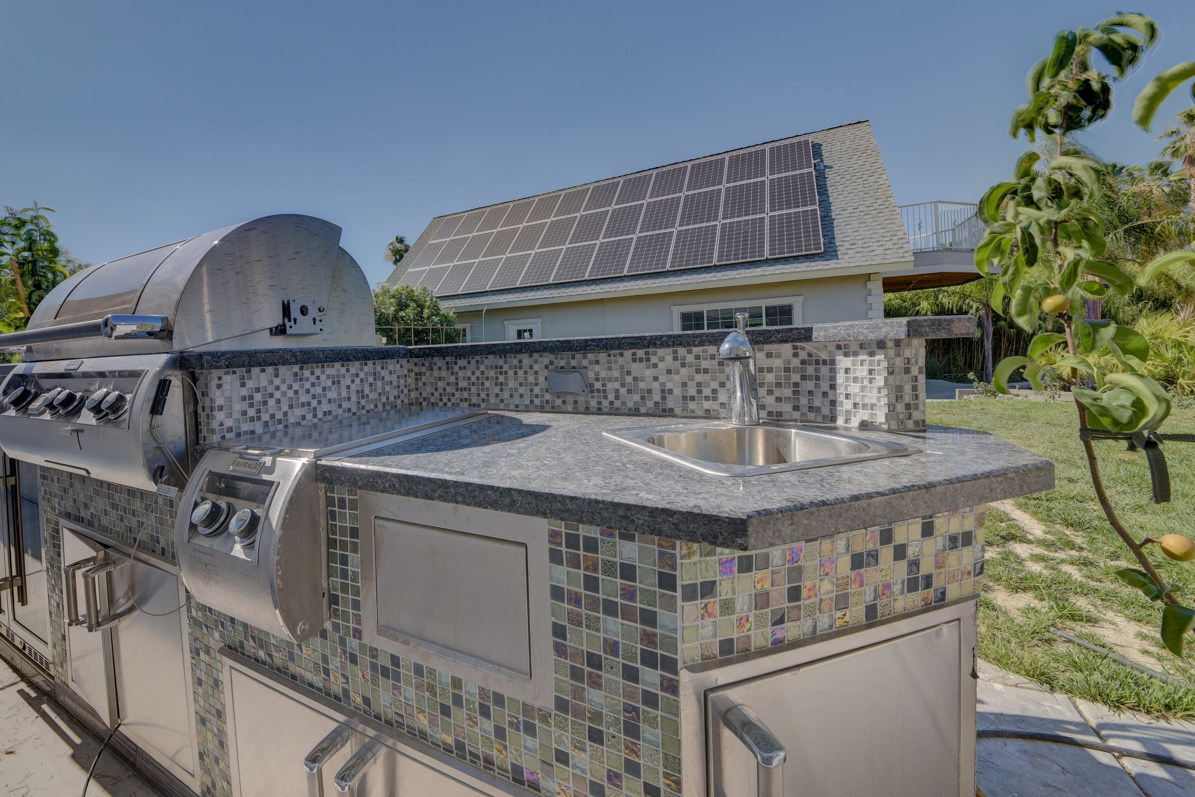 Eine Außenküche mit integriertem Spülbecken und Grill, neben einem Haus mit Solaranlage.