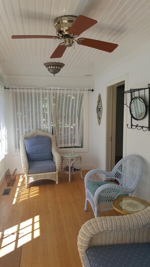 A sunlit room with a ceiling fan, wicker furniture, and a window with sheer curtains. - Sag Harbor Village Gem (Sag Harbor)