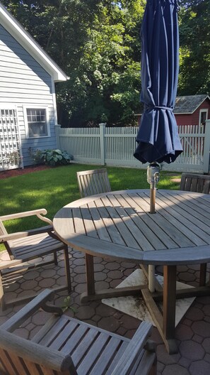 A round wooden patio table with chairs, an umbrella, and a metal table lamp. - Sag Harbor Village Gem (Sag Harbor)