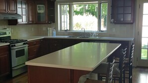 A modern kitchen with a large island, wooden cabinets, and a built-in oven. - Sag Harbor Village Gem (Sag Harbor)