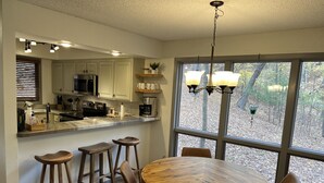 A modern kitchen with white cabinets, a stainless steel range, and a large window overlooking a wooded area. - The Resting Place on Pine Cove at Mountain Harbor (Mt Ida)