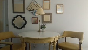 Ein Zimmer mit einem runden Tisch, zwei gelben Stühlen, einer Lampe und mehreren gerahmten Bildern an der Wand.