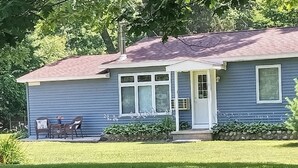 Ein Bungalow mit Veranda, Schornstein und einem kleinen Garten mit Rasen und Sträuchern.