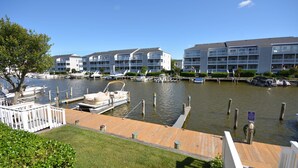A marina with docked boats, a wooden dock, and a building with multiple balconies. - Cozy, inviting 1 bedroom condo with an outdoor pool and gorgeous canal-front view located uptown on the bayside just a few blocks from the beach! (Ocean City)