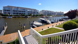 A marina with boats docked, a wooden deck, and a building with multiple balconies. - Cozy, inviting 1 bedroom condo with an outdoor pool and gorgeous canal-front view located uptown on the bayside just a few blocks from the beach! (Ocean City)