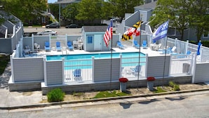 A swimming pool area with a white fence, blue lounge chairs, and flags. - Cozy, inviting 1 bedroom condo with an outdoor pool and gorgeous canal-front view located uptown on the bayside just a few blocks from the beach! (Ocean City)