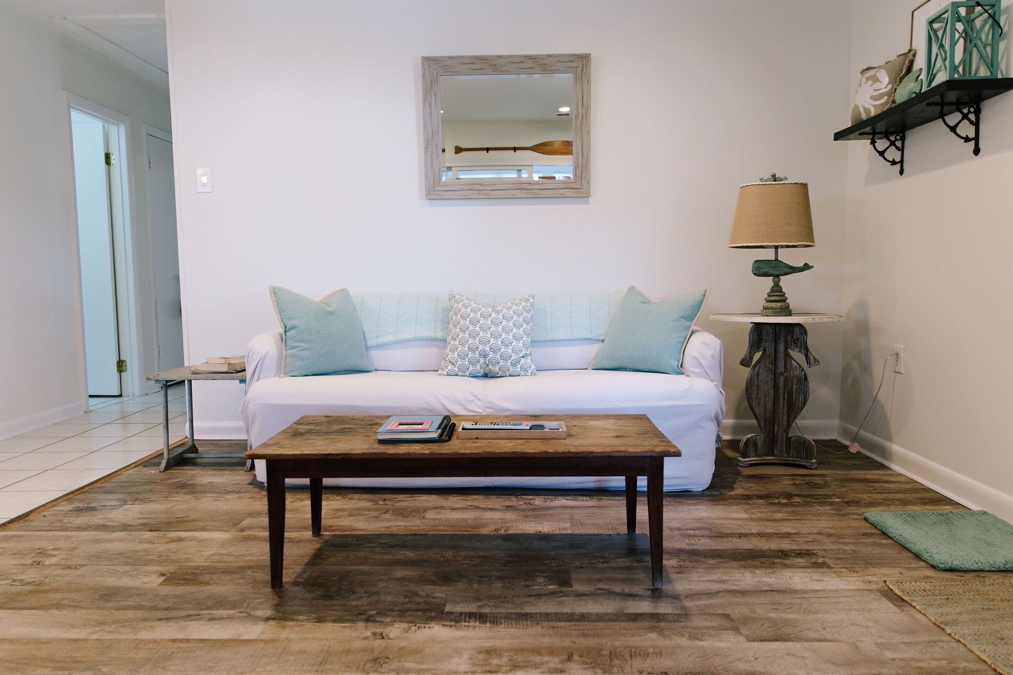 A living room with a white sofa, a wooden coffee table, a lamp, and a mirror on the wall.