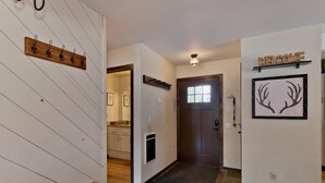 A hallway with a wooden bench, a welcome sign, a framed antler picture, and a tiled floor.