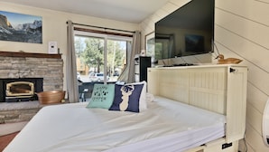 A bedroom with a bed, a fireplace, a TV, and a window with a view of the outside.