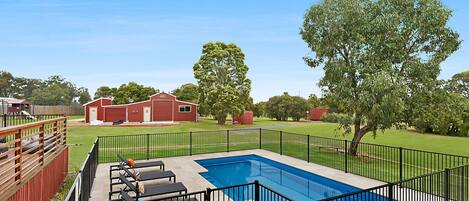 A backyard with a swimming pool, a red barn, and a fenced area with lounge chairs.