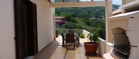 A balcony with a grill, a table with chairs, and a potted plant.