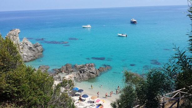 A coastal beach with clear turquoise waters, rocky formations, and boats. - Townhouse with stunning view, only 5 minutes walk to the beach (Vibo Valentia)