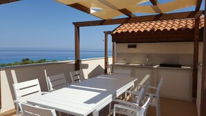 A covered outdoor dining area with a view of the sea, a small kitchen, and white furniture. - Townhouse with stunning view, only 5 minutes walk to the beach (Vibo Valentia)
