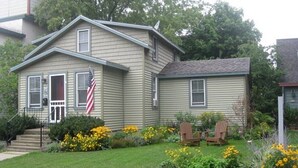A two-story house with a front porch, a small garden with yellow flowers, and two Adirondack chairs. - Locally owned downtown home:  Bar Harbors Crows' Nest (Bar Harbor)