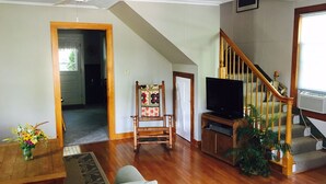A living room with hardwood floors, a wooden staircase, a television, a chair, and a plant. - Locally owned downtown home:  Bar Harbors Crows' Nest (Bar Harbor)