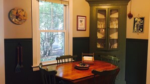A dining area with a wooden table and chairs, a window with blinds, a green cabinet with glass doors, and a wall clock. - Locally owned downtown home:  Bar Harbors Crows' Nest (Bar Harbor)
