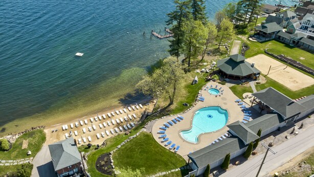 Luftaufnahme eines Sees mit einem Ferienresort, das einen Swimmingpool, einen Strandbereich und mehrere Gästezimmer umfasst.