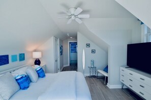 A bedroom with a bed, a TV, a ceiling fan, and a view of a blue door.