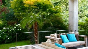 An outdoor seating area with a sofa and cushions, surrounded by lush greenery and a palm tree.