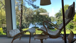 A room with a large window, a hammock chair, a cushioned bench, and a small round table.
