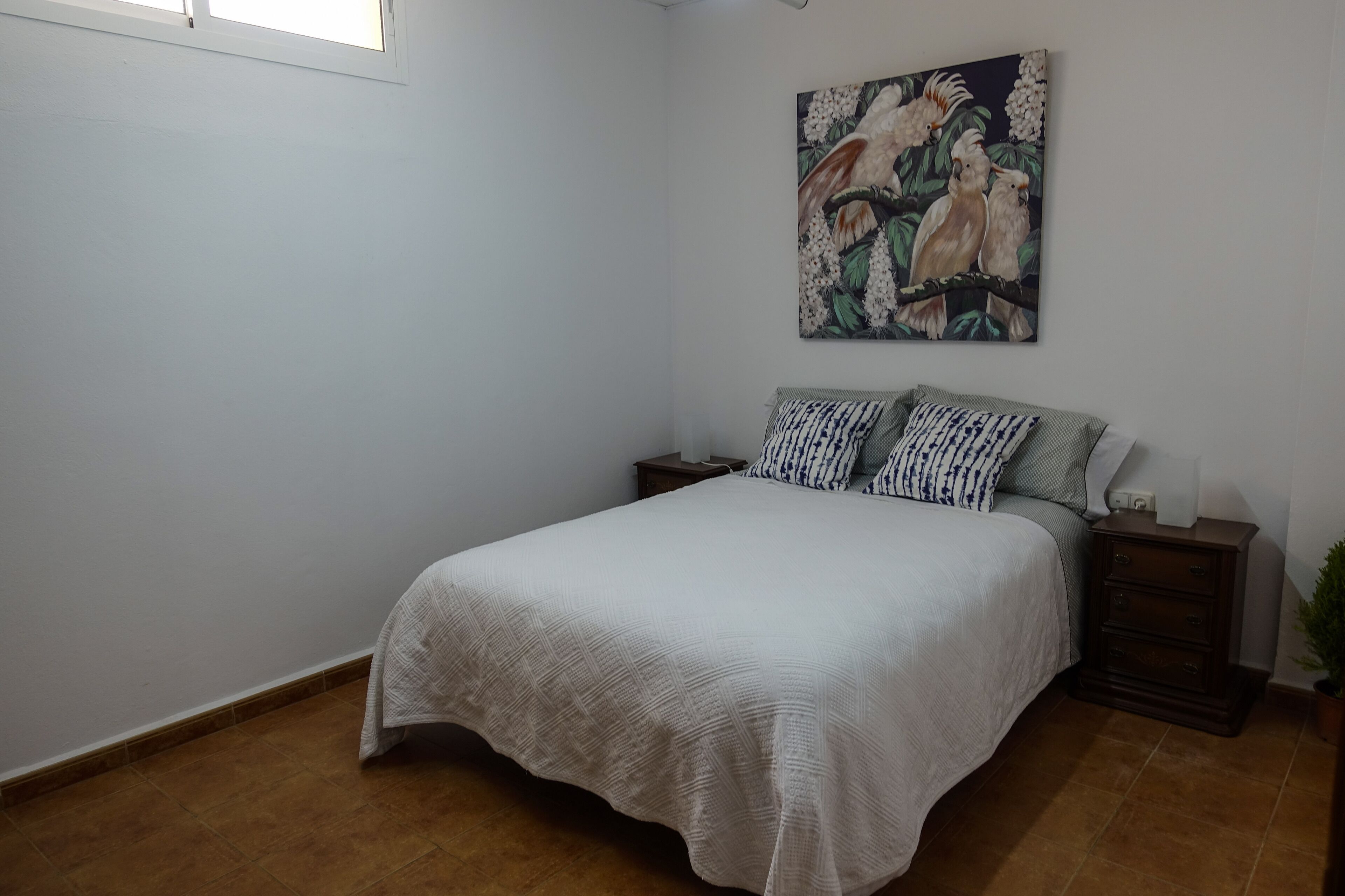 A bedroom with a bed, nightstands, a painting, and a potted plant.