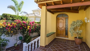 A building with a yellow facade, a wooden door, and a tiled patio.